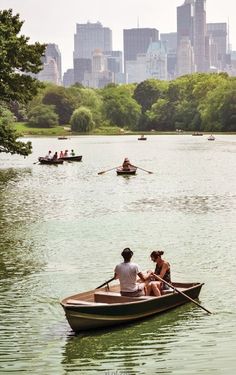 two people in a row boat on a lake with the city skyline in the background