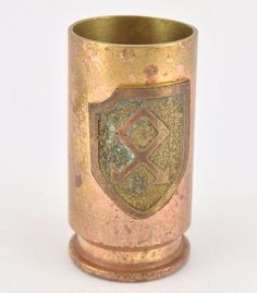 an old brass cup with a shield on the front and sides, sitting on a white surface