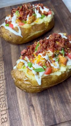 two loaded baked potatoes sitting on top of a wooden cutting board next to each other