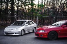 two cars parked next to each other in front of a chain link fence and trees