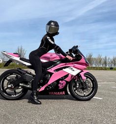 a person sitting on a pink motorcycle in the middle of a parking lot with blue skies behind them