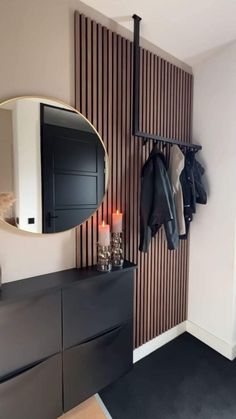 a coat rack with two coats hanging on it next to a wall mounted mirror and candles