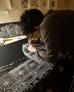 a man writing on a piece of paper in front of a wall covered with drawings