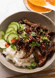 a bowl filled with rice, meat and cucumbers next to chopsticks