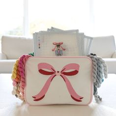 a white purse with pink bow on it sitting on a table in front of a window