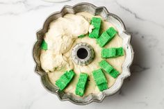 a cake pan filled with white frosting and green sprinkles on top of a marble counter