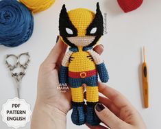 a crocheted wolverine doll being held by someone's hand with scissors and yarn in the background