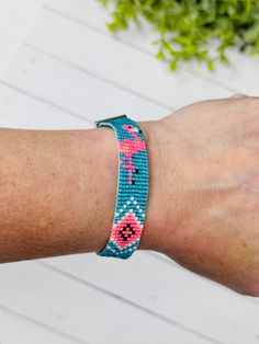 a woman's arm wearing a bracelet with pink and blue beads on it, next to a plant