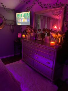 a bedroom with purple lighting and flowers on the dresser next to a tv screen that is turned on