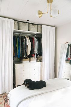 a black dog laying on top of a bed next to a closet filled with clothes