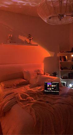 a laptop computer sitting on top of a bed in a room with orange light coming from the ceiling