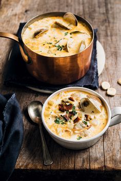 a bowl of soup on a wooden table next to a spoon and some silverware