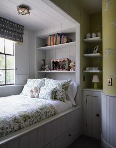 a white bed sitting under a window next to a book shelf filled with books and stuffed animals