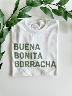 "Buena, Bonita, Borracha Shirt  A play on words from the famous saying \"Bueno, bonito barato\"  T-shirt: Unisex sizing Color: White with olive green font  50% Polyester, 50% Cotton Image is sublimation" Latina T Shirt Ideas, Spanish Shirt Ideas, Chingona T Shirt, Spanish Tshirt Designs, Chingona Shirt, T Shirt Sublimation, Green Font, Spanish Shirts, T Shirt Ideas