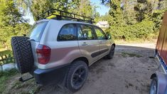 a silver car parked on the side of a dirt road next to a red truck