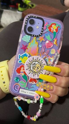 someone is holding up their phone case with some stickers on it and yellow nails