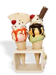 two ice cream cones with toppings sitting on a small shelf, one has an umbrella and the other has cherries