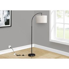 a floor lamp with a white shade on it in front of a gray wall and wooden floor