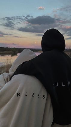 two people sitting on a bench looking out at the water and grass in the distance