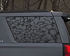 the back end of a gray car with flowers on it's side window decal