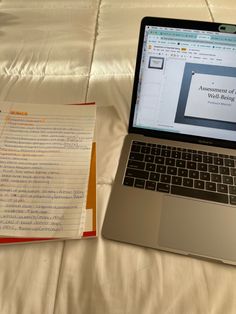 an open laptop computer sitting on top of a bed next to a paper workbook