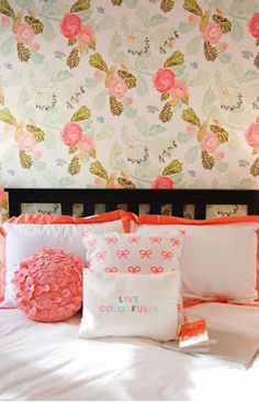 a bed topped with lots of pillows next to a wallpapered headboard covered in flowers