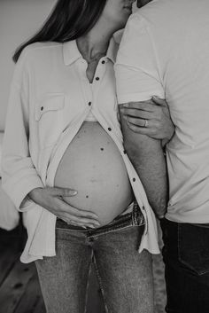 a pregnant woman standing next to a man with her belly tucked under her shirt and holding her hand on her stomach