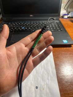 a hand is holding a black and green cord in front of a laptop