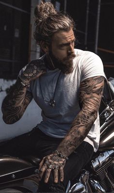 a man with long hair and tattoos sitting on a motorcycle