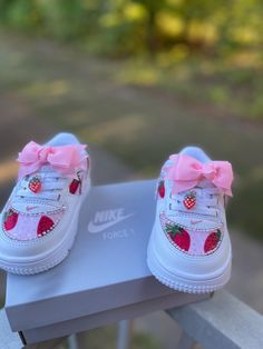 a pair of white sneakers with pink bows on them sitting on a box outside in the sun