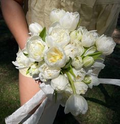 a bouquet of white tulips is held by a bride's hand on the grass