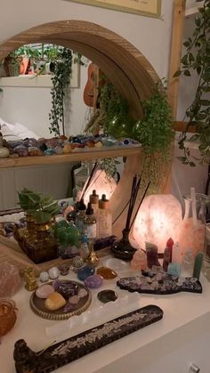 a table topped with lots of different types of items next to a mirror and potted plant