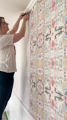 a woman is painting a wall with colorful flowers on it and she is holding a paint roller