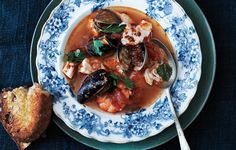 a bowl of stew with clams and bread on a plate, ready to be eaten