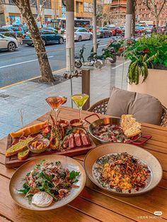 a wooden table topped with plates of food next to a sidewalk filled with parked cars