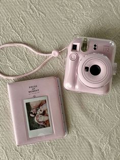 a pink camera sitting on top of a bed next to a photo album with a baby's picture in it