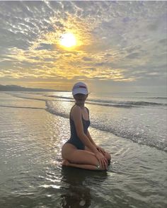 a woman sitting on top of a surfboard in the middle of the ocean at sunset