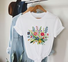 Please note that this shirt is a PRINTED version, meaning that the embroidery design is printed on a flat surface rather than being physically embroidered. While it may not have the tactile feel of actual embroidery, the printed design still adds a touch of elegance and style to the shirt. Trending right now printed embroidery tshirts for women, Garden Shirt, Wildflower Shirt, Floral Tee, Flower Tshirt, Vintage Wildflowers, Wild Flowers Shirt, Vintage Floral Shirt, Botanical Tshirt, Dainty Flowe Multicolor Floral Embroidery T-shirt For Summer, White Floral Embroidered T-shirt For Spring, Spring Embroidered Cotton Shirt, Multicolor Floral Embroidered T-shirt For Summer, Casual Multicolor Floral Embroidery T-shirt, Casual Multicolor T-shirt With Floral Embroidery, Embroidered Cotton Shirt For Spring, Spring Short Sleeve Shirt With Embroidered Graphics, Casual Multicolor Floral Embroidery Shirt