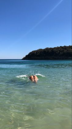 a man swimming in the ocean with his head above the water's surface and an island in the distance