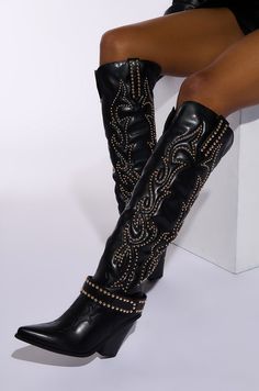 Kick your looks up a notch when you top them off with The AZALEA WANG Maitia Black Embellished Western Boot. This standout faux leather style features a pointed toe silhouette, a stacked chunky heel with a notched accent, tonal stitching, a sexy knee-high shaft with front and back vented cut outs, Western-inspired embroidered stitching, and faux gold metallic circular studded embellishments. Complete with a detachable studded velcro belt at the base, embellished side pull tabs, and a pull on fit. Style with mini skirts and faux leather fringe jackets for an elevated finish.   (all measurements are approximate from size 7.5) - Faux Leather Upper - Pointed Toe - Stacked Chunky Heel - Knee-High Shaft - 3.75” Heel Height - 17.75” Shaft Height - 16.25” Top Shaft Circumference - Imported  Produc Festival Maxi Skirt, Rhinestone Blouse, Bodycon Maxi Skirt, Fringe Leather Jacket, Azalea Wang, Chunky Sandals, Flatform Sandals, Western Boot, Wedge Heel Sandals