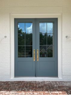 two blue double doors with gold handles and sidelights in front of a white brick building