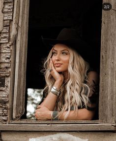 a woman with long blonde hair wearing a black cowboy hat and looking out the window