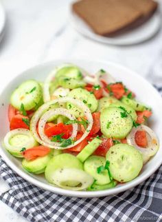 a white bowl filled with cucumber, tomatoes and onion salad on top of a table