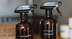 two brown spray bottles sitting next to each other on a wooden table with boxes in the background