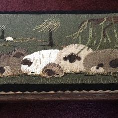 a cat is laying down on the ground in front of a rug with sheep and trees