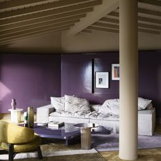 a living room with purple walls and white furniture on the floor, along with two yellow chairs