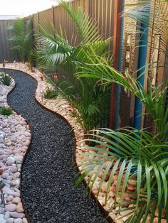 a garden with rocks, plants and gravel in front of a fenced in area