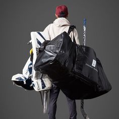 a man carrying a large black bag with skis on it's back and poles in his hand