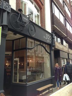 a woman walking past a store front with a bicycle on the window sill and people walking by