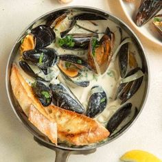 a pan filled with mussels and sauce on top of a table next to lemon wedges